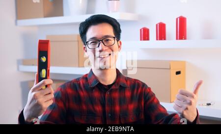 Young asian handyman showing thumb up and holding leveller in the other hand. High quality photo Stock Photo