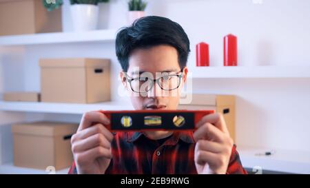 Young asian handyman holding leveler indoors. High quality photo Stock Photo