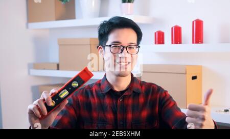 Young asian handyman showing thumb up and holding leveller in the other hand. High quality photo Stock Photo