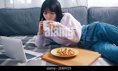 Young asian woman speaking on the phone while drinking coffee and eating breakfast. High quality photo Stock Photo