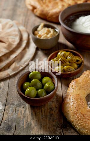 Tasty breakfast with green olives, fresh mozzarella cheese in brine, chick pea spread, sesame bagel and flat bread in a vertical view on rustic table
