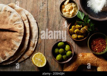 Breakfast still life with fresh sesame bagel, green olives, chick pea paste and flat bread in an overhead view on a wooden table served with a twist o Stock Photo