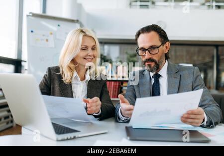 Happy friendly colleagues learning financial document for business plan. Successful influential mature coworkers working on corporate project, discuss some ideas, partnership concept Stock Photo