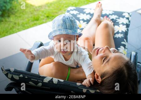 Pretty loving mom trying to soothe scarred crying baby and get rid of baby's fear by holding her in mother's arms, hugging and smiling happily Stock Photo