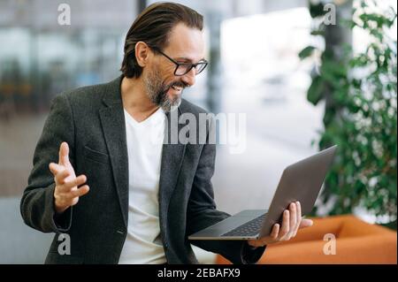 Happy male employee on video conference with colleagues, discuss work process. Joyful senior businessman using laptop, is having online briefing meeting, distant work concept Stock Photo