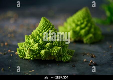 some raw baby romanesco broccoli heads on a dark stone surface sprinkled with different herbs, spices and seeds Stock Photo