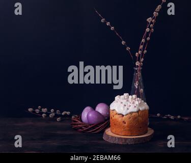 Easter cakes on a dark background, decorated with marshmallows and painted Easter eggs in a wicker nest. Stock Photo
