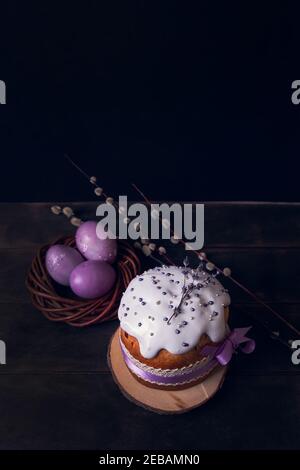Easter cakes on a dark background, decorated with lavender and marshmallows, and painted Easter eggs in a wicker nest. Stock Photo