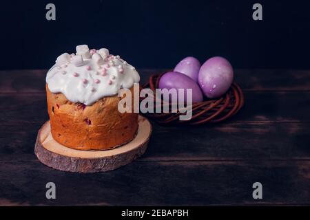 Easter cakes on a dark background, decorated with marshmallows and painted Easter eggs in a wicker nest. Stock Photo