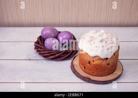 Easter cakes decorated marshmallows, and painted Easter eggs in a wicker nest on a light wooden background. Stock Photo