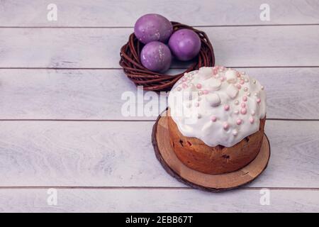 Easter cakes decorated marshmallows, and painted Easter eggs in a wicker nest on a light wooden background, top view copy space. Stock Photo