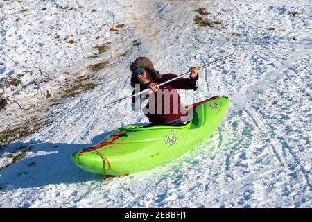 Edinburgh, Scotland, UK. 12 Feb 2021.  As the cold weather continues members of the public are out in Holyrood Park playing sport and making political slogans. Pic; A man in a canoe hurtles down a snow covered hillside at the foot of Arthur’s Seat . Iain Masterton/Alamy Live news Stock Photo
