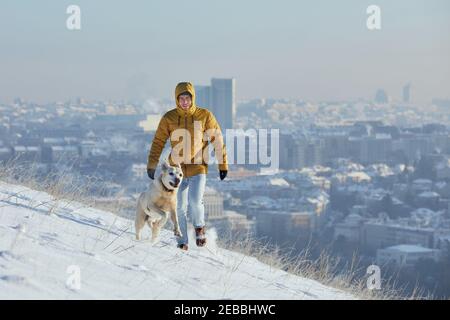 Happy young man with dog in winter. Pet owner with his labrador retriever walking in snow against city. Prague, Czech Republic Stock Photo