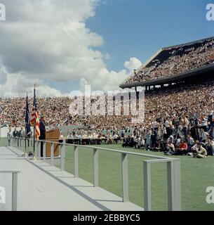 Inspection tour of NASA installations: Houston, Texas, motorcade, address at Rice University, 9:34AM. President John F. Kennedy (left, at lectern) delivers remarks at Rice University regarding the nationu0027s efforts in space exploration. White House Secret Service agent, Roy Kellerman, stands at far left. Members of the press sit in background; photographers gather at right; spectators observe from the stands. Rice University Stadium, Houston, Texas. Stock Photo