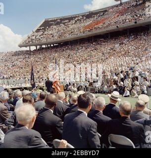 Inspection tour of NASA installations: Houston, Texas, motorcade, address at Rice University, 9:34AM. President John F. Kennedy (left, at lectern) delivers remarks at Rice University regarding the nationu0027s efforts in space exploration. Members of the press sit at left in background; photographers gather at right; spectators observe from the stands. Rice University Stadium, Houston, Texas. Stock Photo