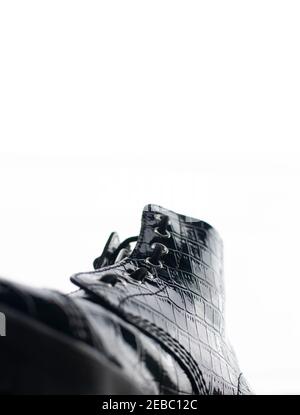 Glossy black shoe with high rubber sole and laces viewed from the front sideways, looking up, against a white background Stock Photo