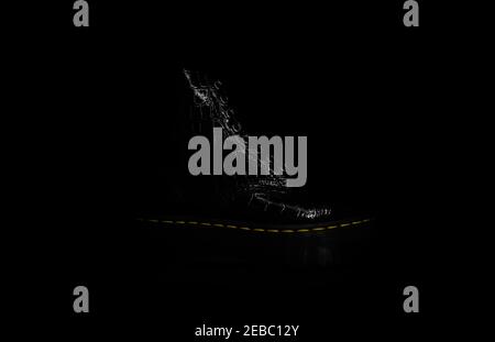Side view of a shiny black shoe with high rubber sole, laces and yellow stitching on black background. Background for ad Stock Photo