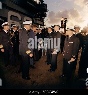 Trip to Western States: Visit to the Pacific Fleet, President Kennedy aboard the USS Kitty Hawk, 5:00PM. President John F. Kennedy (center) shakes hands with an unidentified U.S. Navy lieutenant aboard the aircraft carrier USS Kitty Hawk (CVA-63), at sea off the coast of San Diego, California. Standing left of President Kennedy in foreground (left to right): Commander-in-Chief of the Pacific Fleet (CINCPACFLT), Admiral John H. Sides; Naval Aide to the President, Captain Tazewell T. Shepard, Jr.; Commander of Carrier Division One, Rear Admiral Paul Masterton (facing away). Stock Photo