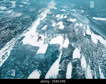 Top view drone shot of man at bicycle riding on the frozen lake with ice texture. Stock Photo