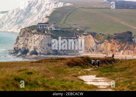 Rugged coastline of Isle of Wight featuring Freshwater bay, promontories, cliffs and beaches. A couple os hiking on the hill on a trail among vast gra Stock Photo