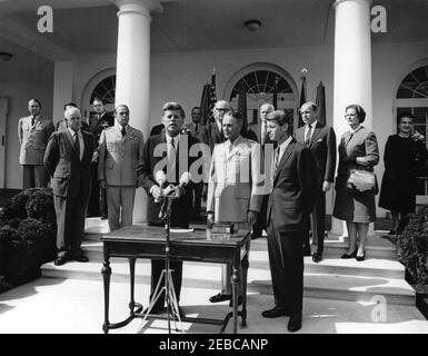 Swearing-in ceremony, Gen. Maxwell Taylor, Chairman, JCS, 12:00PM. President John F. Kennedy delivers remarks during the swearing-in ceremony of General Maxwell D. Taylor as Chairman of the Joint Chiefs of Staff (JCS). Standing in foreground (left to right): President Kennedy (at microphones); General Taylor; Attorney General, Robert F. Kennedy. Looking on from the steps of the West Wing Colonnade, beginning at the very back (left to right): Military Aide to the President, General Chester V. Clifton; Air Force Aide to the President, Brigadier General Godfrey T. McHugh (mostly hidden); Naval Ai Stock Photo