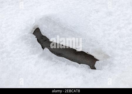 Dark thawed patch in ice covered with snow, winter lake surface Stock Photo