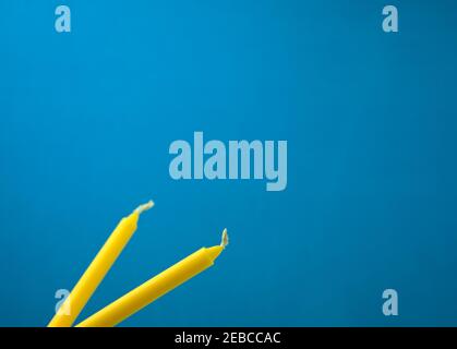 Bright yellow candles isolated on blue background. Off-center, head on, side view composition shot. Horizontal frame. Copy space. Stock Photo