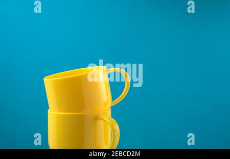 Glossy yellow colored cups stacking on blue background. Off-center, head on, side view composition shot. Horizontal image. Copy space. Stock Photo