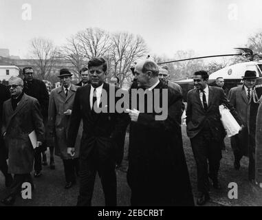 Welcoming ceremony upon the return of the US Delegation to the Punta del Este Conference, 2:10PM. President John F. Kennedy walks to the White House with Secretary of State Dean Rusk as Secretary Rusk and other delegates return from the Punta del Este Conference in Uruguay. Special Assistant to the President Richard u201cDicku201d Goodwin (carrying white bag) walks at right. Secret Service agents Win Lawson (left of the President, wearing hat) and Ernie Olsson (near helicopter) follow with reporters. Falling snow is visible. South Lawn, White House, Washington, D.C. Stock Photo