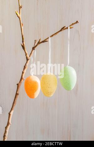 Three pastel colored Easter eggs on branch on wooden vintage background in spring. Minimalistic of Eastern decoration. Easter mood decoration. Vertica Stock Photo