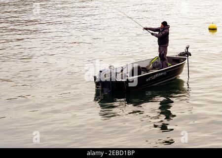 ng rod on the lake Zurich in winter. He is standing in a boat and there is a yellow buoy on the water surface around him. Stock Photo