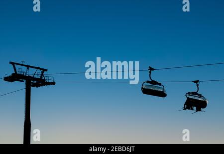 Chair ski lifts in silhouette against a clear evening sky. Stock Photo