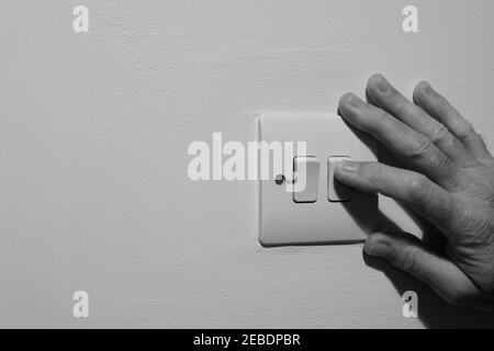 A Double Wall Light Switch, Showing a Natural Elderly Hand Switching off the Power Supply to Save Electricity in the UK. Stock Photo