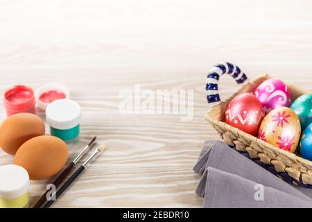 Multicolored easter painted handmade eggs, paints and brushes. Festive Easter frame from eggs, paints and brushes on white wooden background with copy Stock Photo