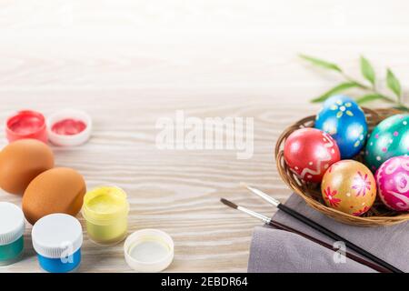 Multicolored easter painted handmade eggs, paints and brushes. Festive Easter frame from eggs, paints and brushes on white wooden background with copy Stock Photo