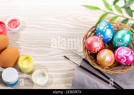 Multicolored easter painted handmade eggs, paints and brushes. Festive Easter frame from eggs, paints and brushes on white wooden background with copy Stock Photo