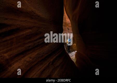 A man is seen through a small slit of red rock inside a canyon Stock Photo