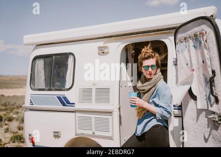 A stylish young woman drinks coffee outside of her trailer in the sun Stock Photo