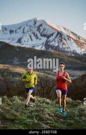 A woman and man trail run at sunset with snowy peak in the distance Stock Photo