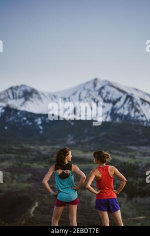 Two female friends stop to chat while trail running in the mountains Stock Photo
