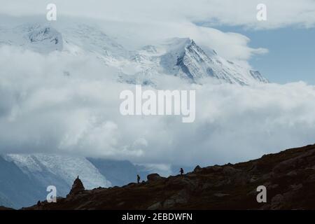 Two hikers walk in the distance up in the clouds and snowy peaks Stock Photo