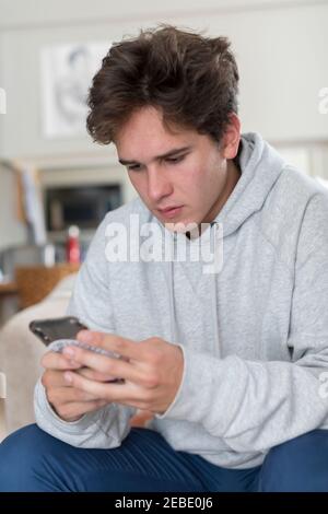 Caucasian male college student sitting indoors texting on cell phone Stock Photo
