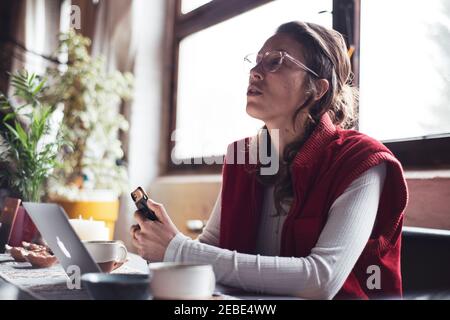 woman talks during meeting at home with phone and laptop in pandemic Stock Photo