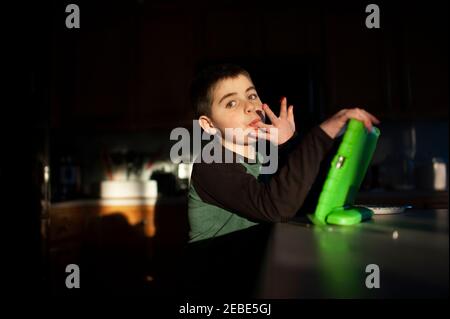 Boy 9-10 years old licks fingers while holding tablet in pretty light Stock Photo