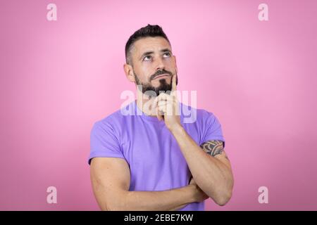 Young handsome man wearing casual t-shirt over pink background with hand on chin thinking about question, pensive expression. smiling and thoughtful f Stock Photo