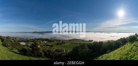 A panorama view of rolling hills landscape in Andalusia with many wind turbines above the fog in the valleys and blue sky above Stock Photo