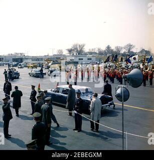 Arrival ceremony for Sylvanus Olympio, President of Togo, 11:00AM. A bubbletop limousine, carrying President John F. Kennedy and President Sylvanus Olympio of Togo, drives through the Military Air Transport Service (MATS) Terminal at Washington National Airport, following arrival ceremonies for President Olympio. White House Secret Service agent, Roy Kellerman (wearing hat), walks along right side of car. US Marine Band plays in background. Washington, D.C. Stock Photo