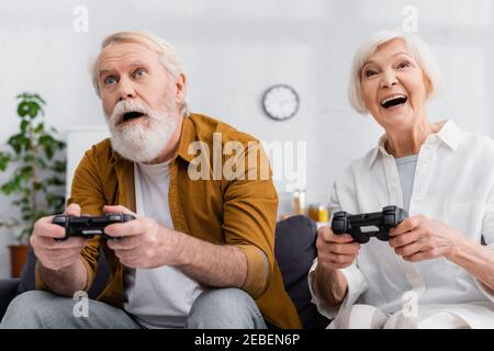KYIV, UKRAINE - DECEMBER 17, 2020: Excited elderly couple playing video game together at home Stock Photo