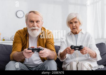 KYIV, UKRAINE - DECEMBER 17, 2020: Elderly couple playing video game at home Stock Photo