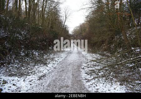 View looking down the snow covered Worth Way towards a brick road bridge crossing the bridleway near the village of Crawley Down in West Sussex, UK. Stock Photo